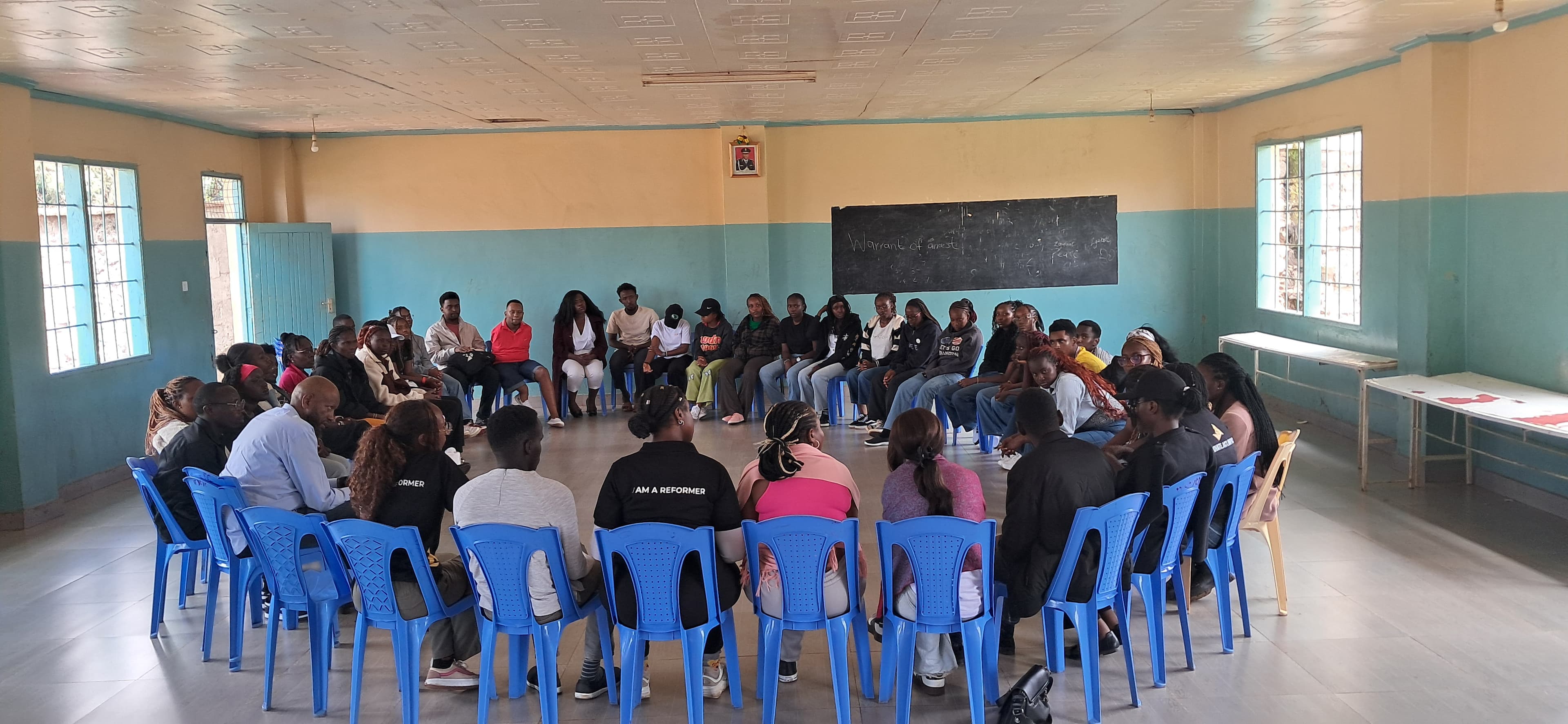 Young people gathered in a bright hall for a conversation, listening to a speaker.